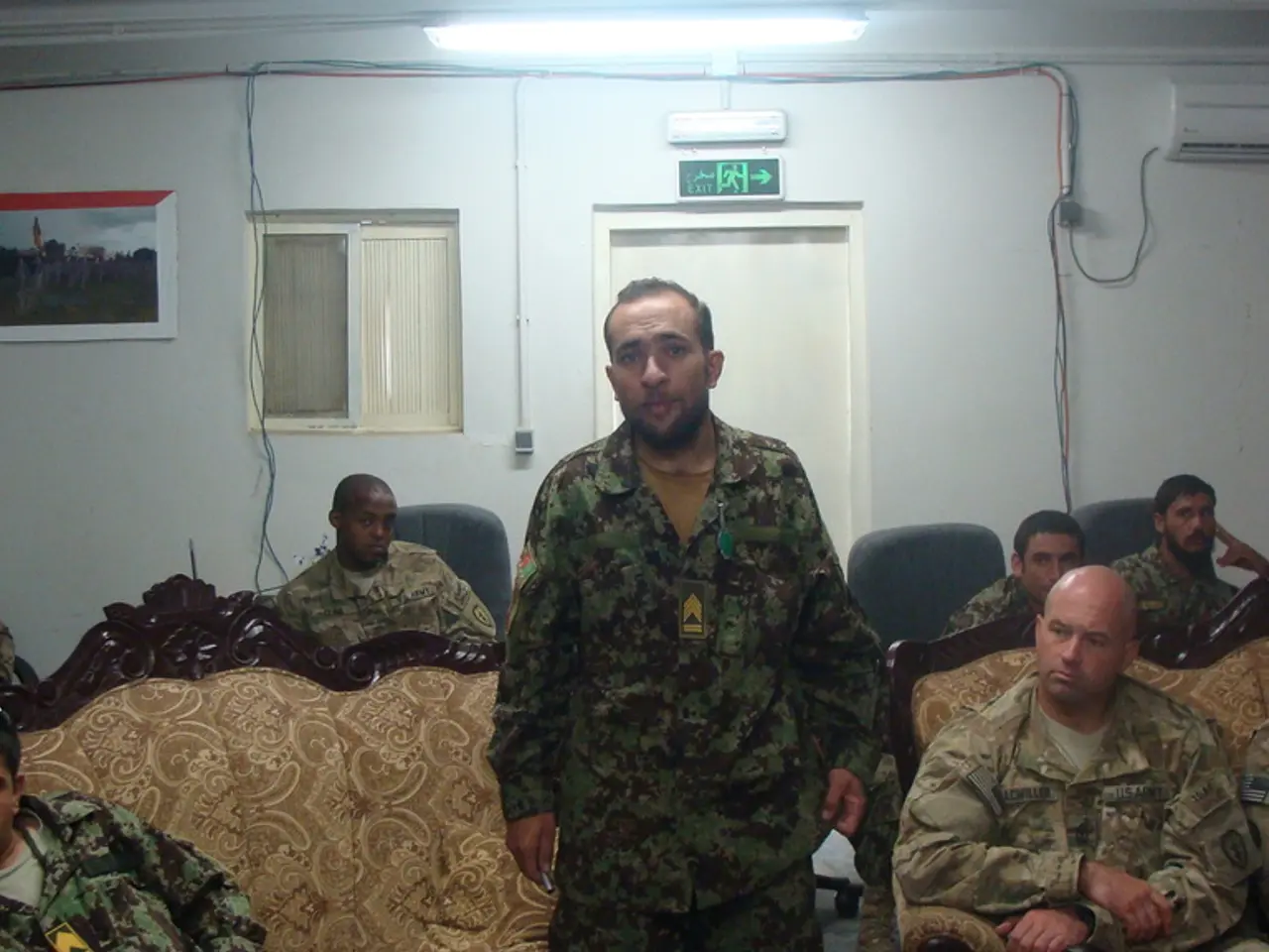 In this picture we can see some army people are sitting in the chairs and couch, among them one...