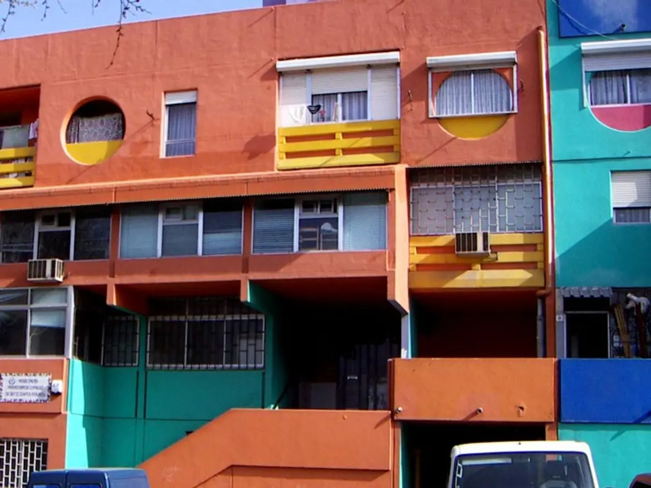 As we can see in the image there are buildings, fence, vehicles and a sky.