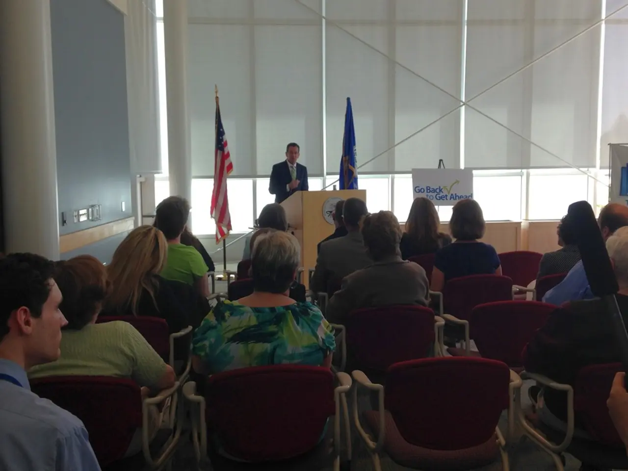 There are many people sitting in the chairs in this room and one guy is standing near the podium...