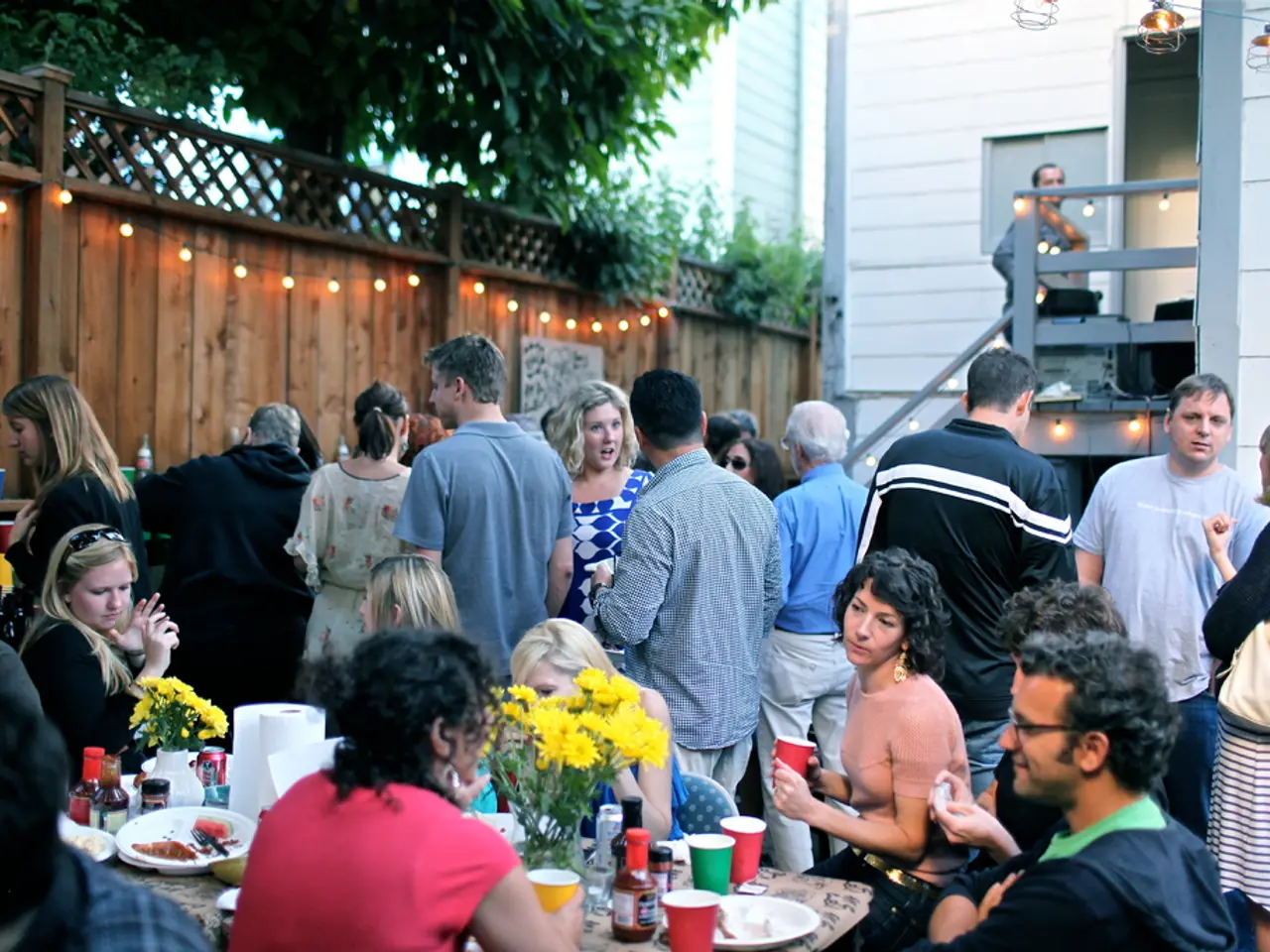 People are at a party. In which some are sitting around a table and some are standing.