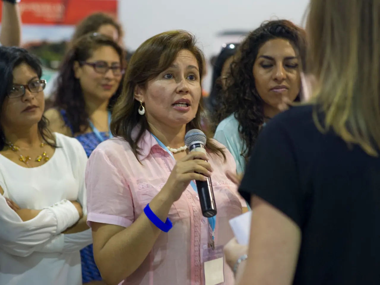 In this image a group of women facing towards the right among which one woman in the center is...