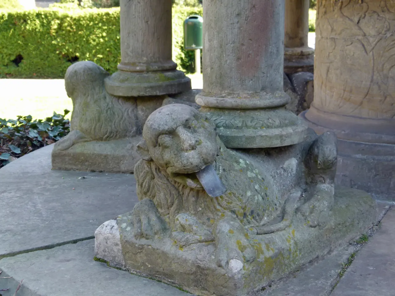 In this image there are poles and depiction of lions. In the background there are trees and leaves...