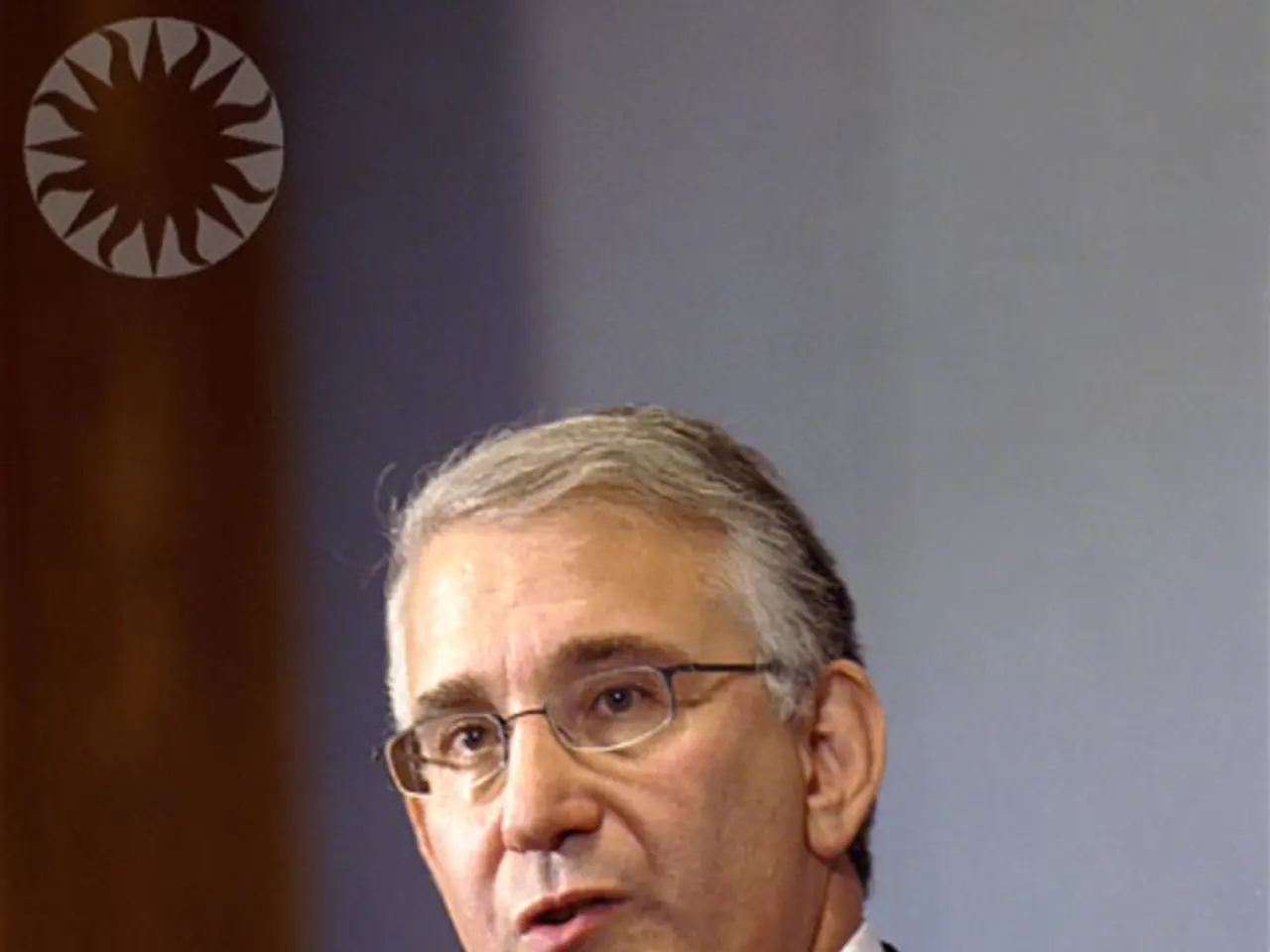 In this picture we can see a man, he wore spectacles, and he is speaking in front of the...