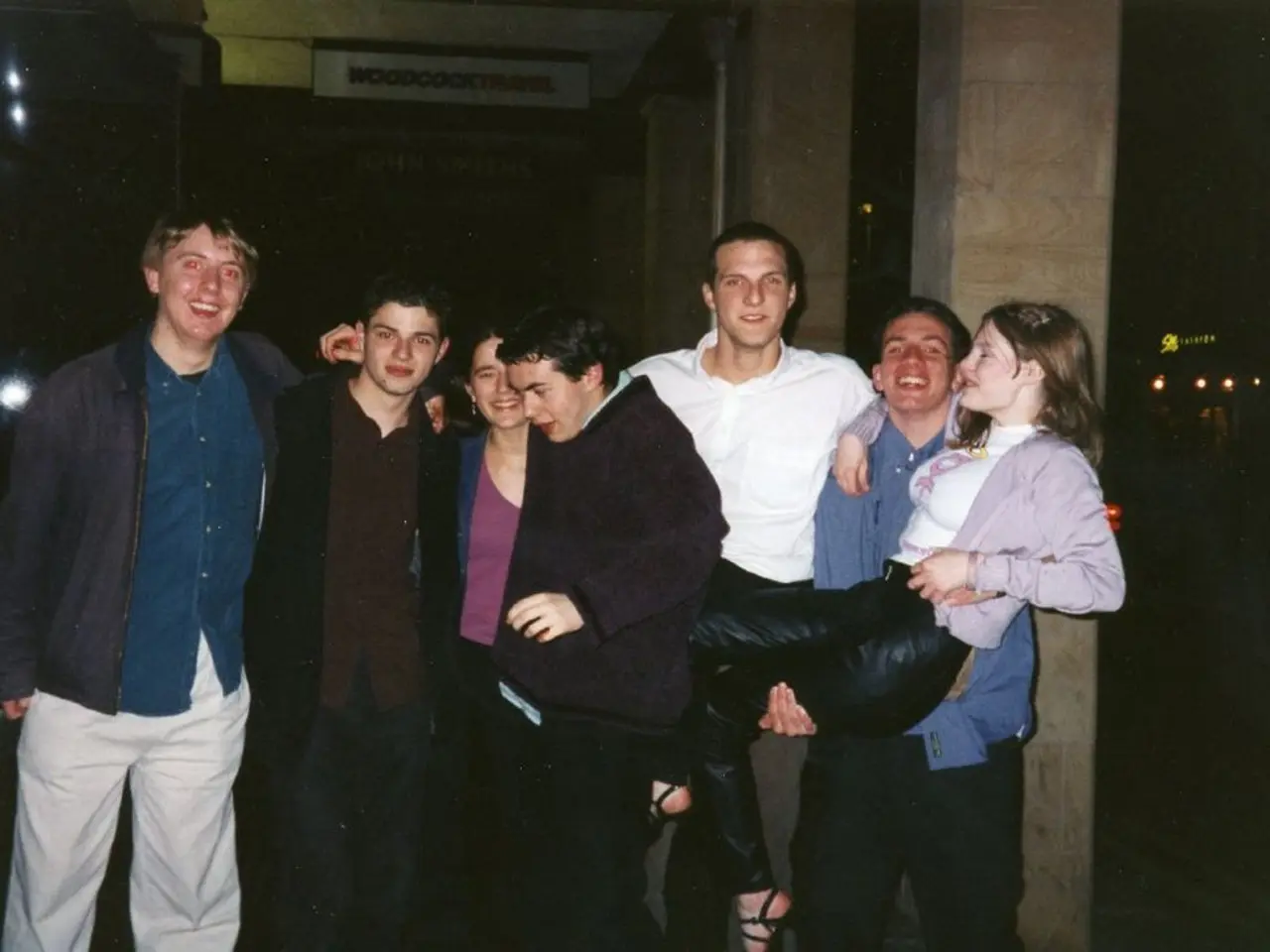 In this image I can see few persons standing and there is a man carrying a woman. There are pillars...