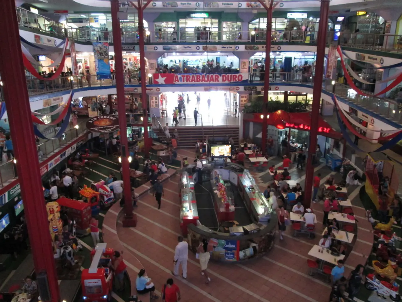 This image is taken in the mall. In this image we can see pillars, persons, tables, floors, flags,...