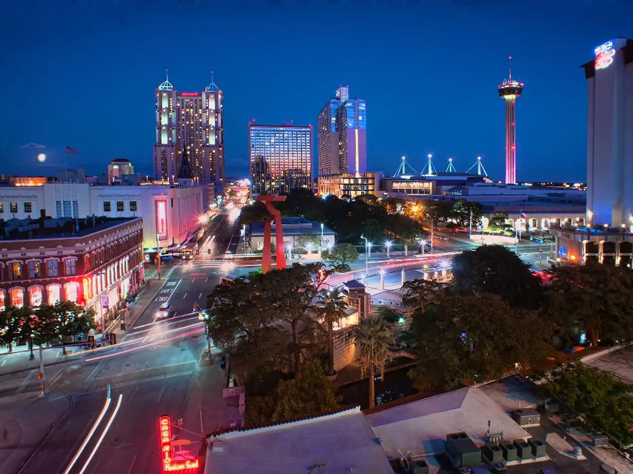 This is the top view of a city, in this image we can see trees, vehicles on the roads, buildings...