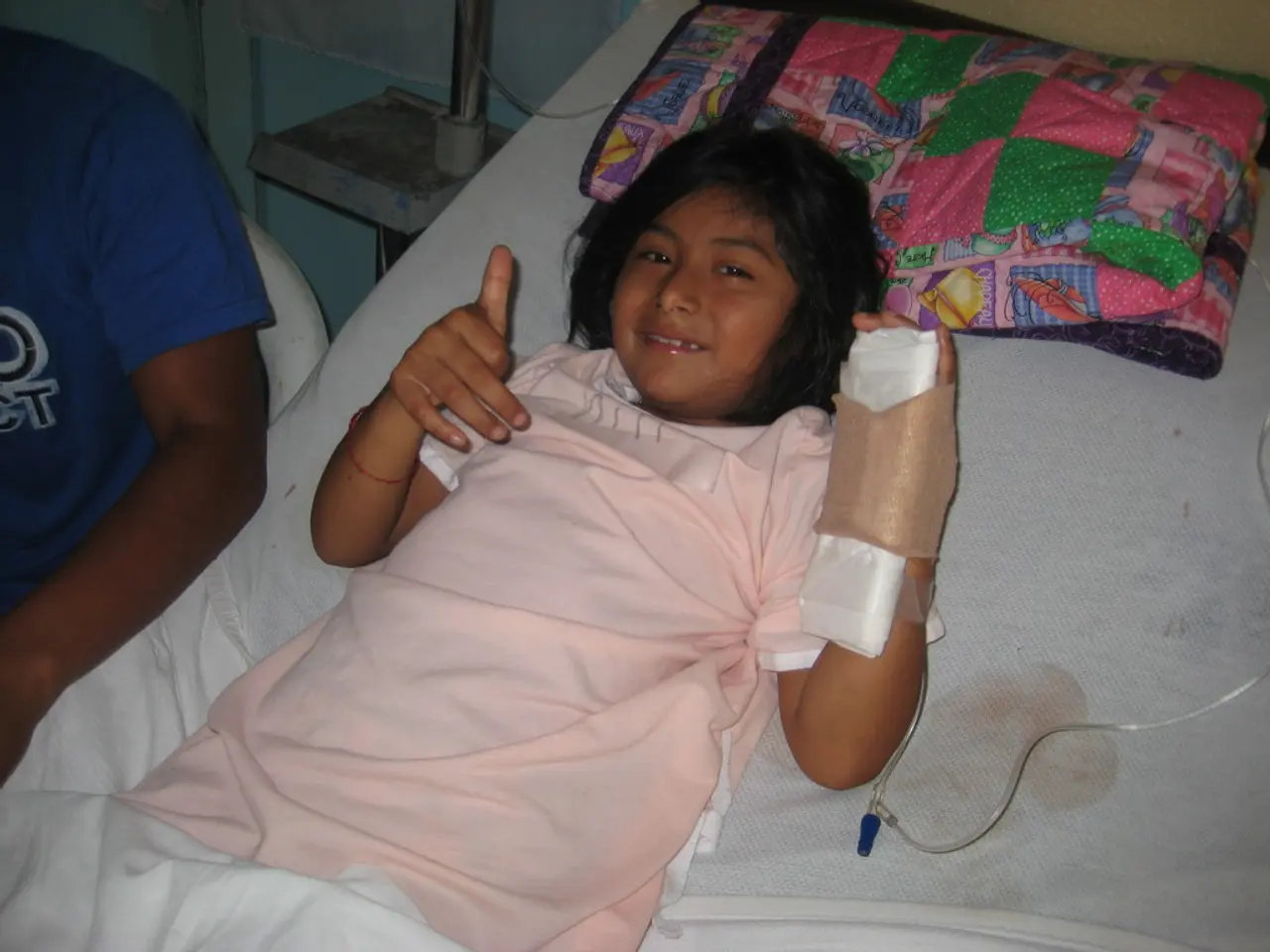 In this picture, we see a girl lying on the bed and she she is having saline in her hand. She has...