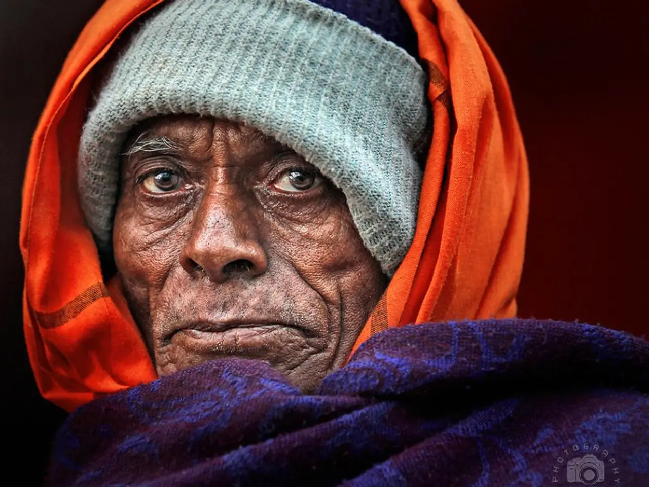 In the image there is an old person. At the bottom there is purple cloth. And on the person head...