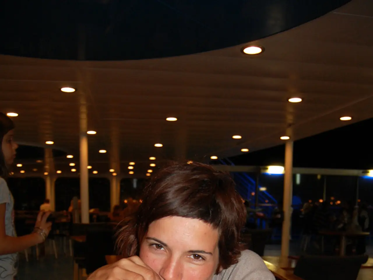 There is a woman sitting on a chair and she is drinking a beer which is on this wooden table. Here...