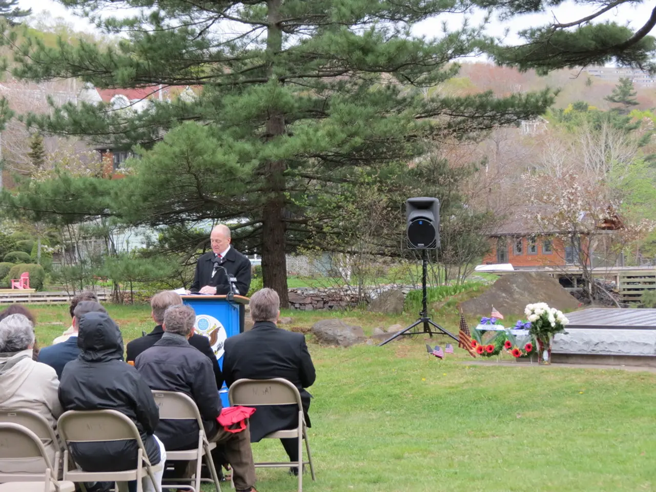 In the image we can see there are people sitting on the chairs and there is a man standing near the...