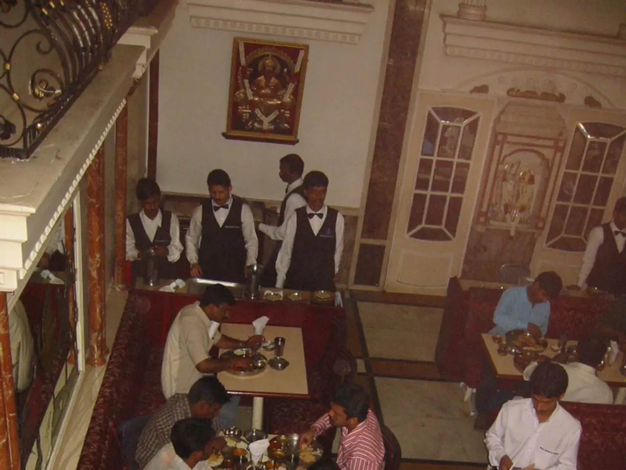 There are so many sitting in a chairs and eating food on tables and few people standing at one...