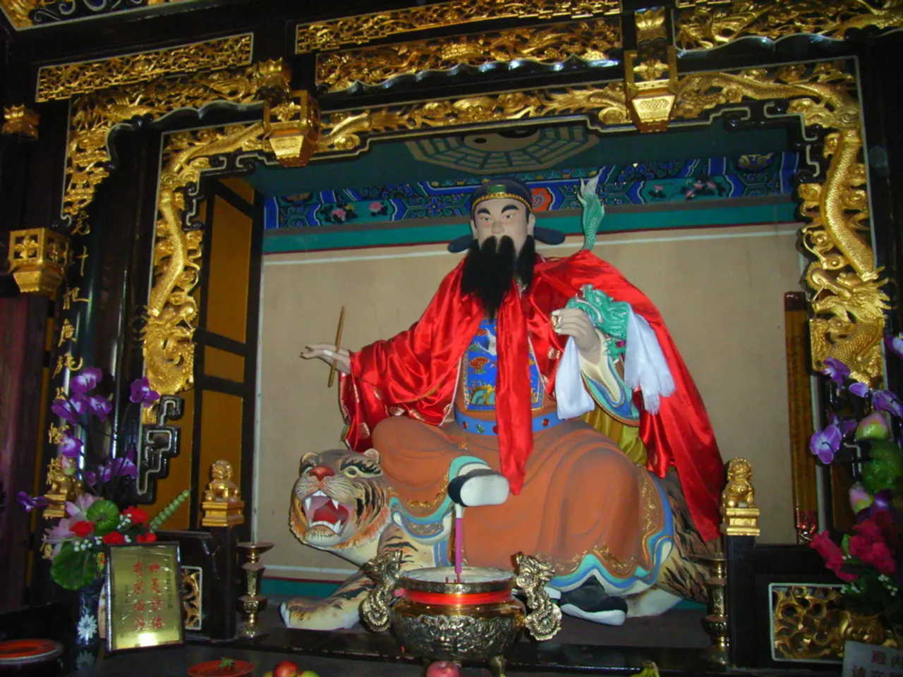 In the image there is a statue of chinese monk with colorful cloth around him sitting on a tiger...
