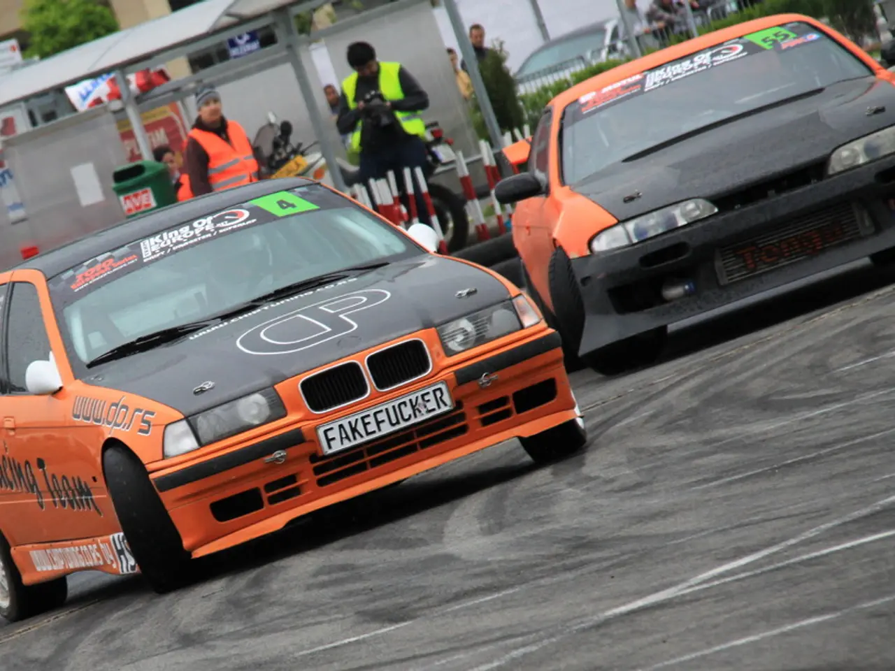 In the image there are two cars drifting on the road, behind it there are few men standing in front...