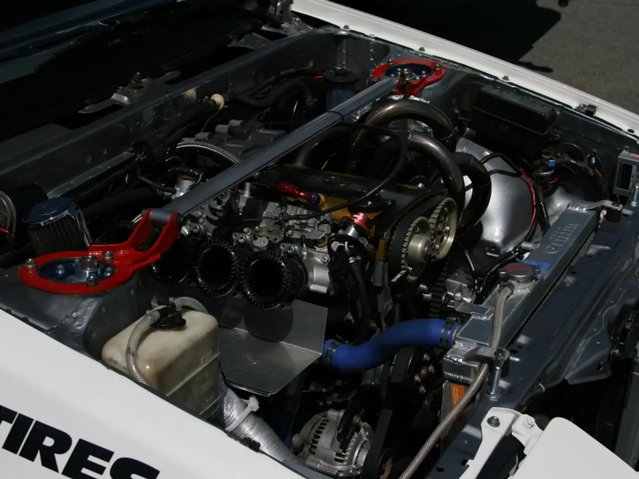 In the picture we can see a car engine with pipes, battery in it.