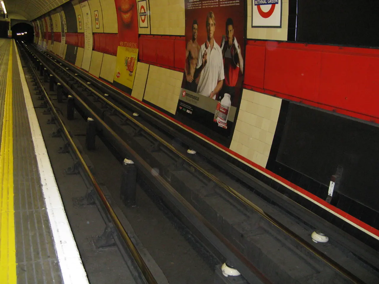 Here we can see a train track. Posters are on the wall.