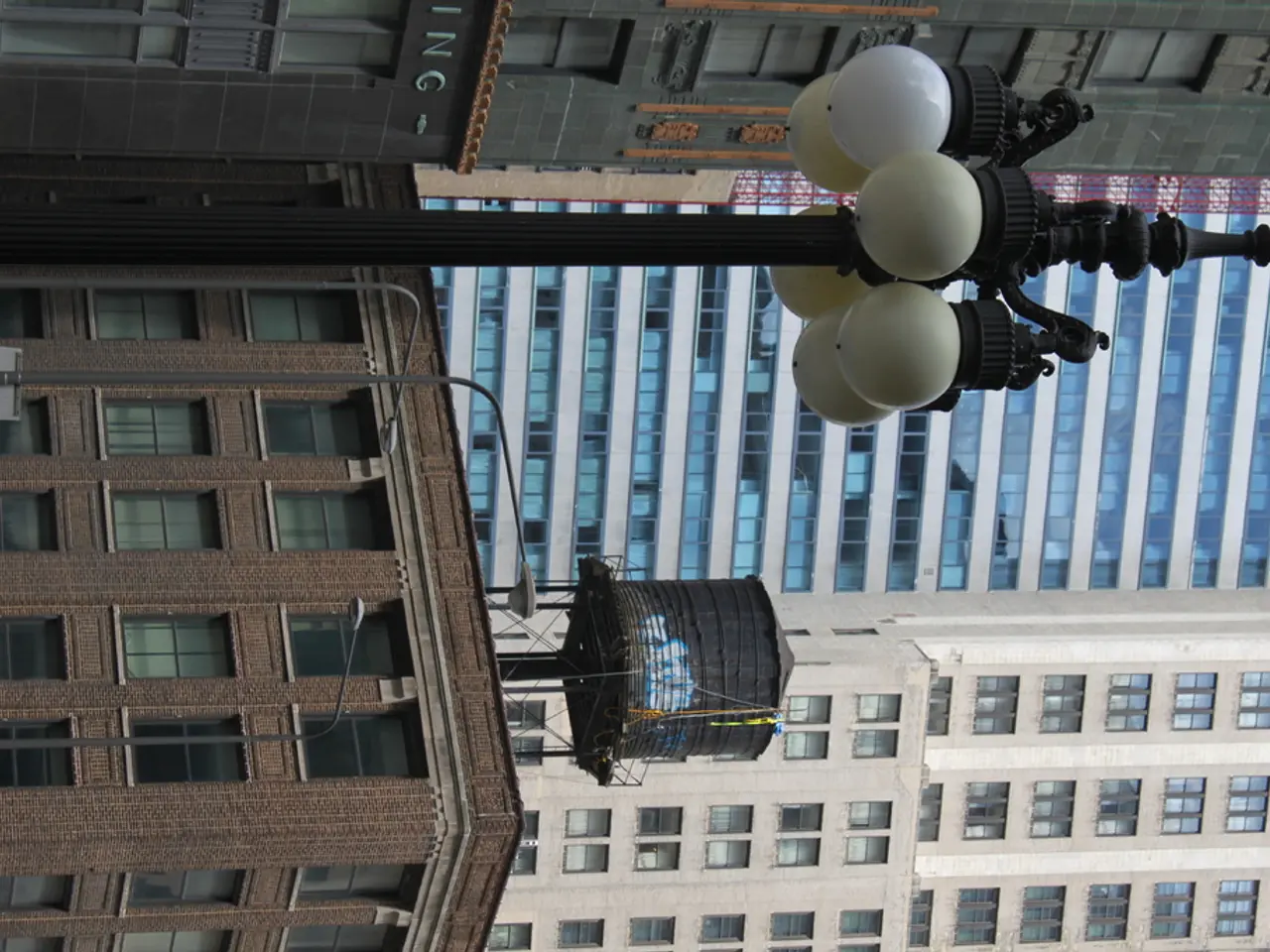 In this image we can see a few buildings, there are some poles, lights and windows, at the top of...