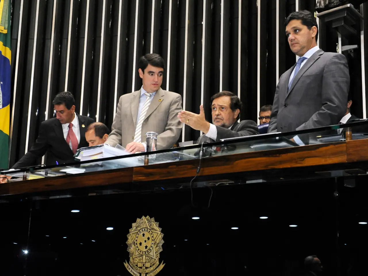 In this picture we can see some people sitting on the stage table. Behind we can see the wooden...