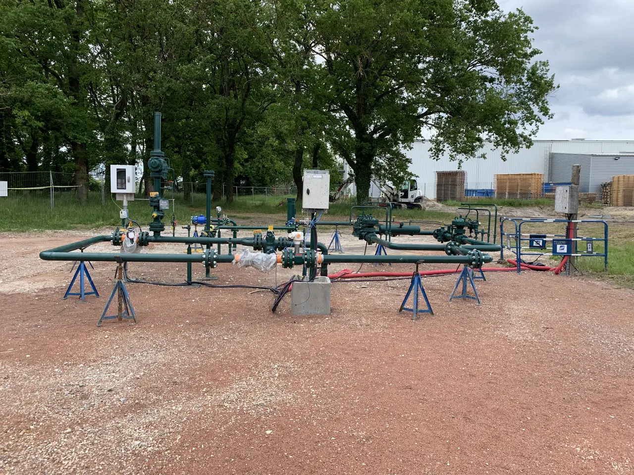 The image shows a large group of pipes and valves sitting on top of a dirt field surrounded by...