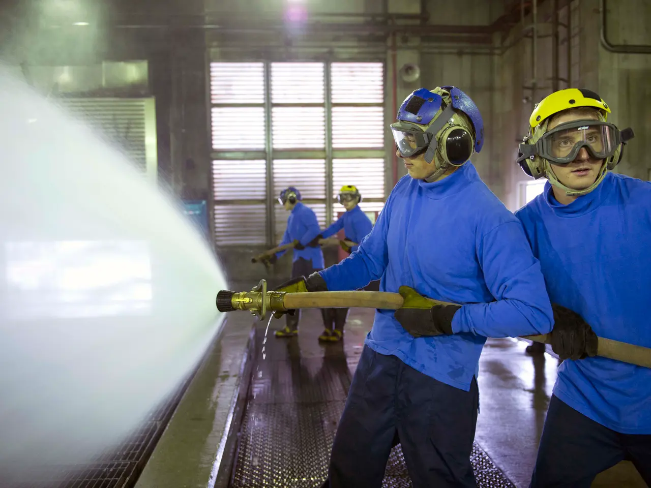 The image shows a group of men in blue shirts and yellow helmets working on a machine, with one of...