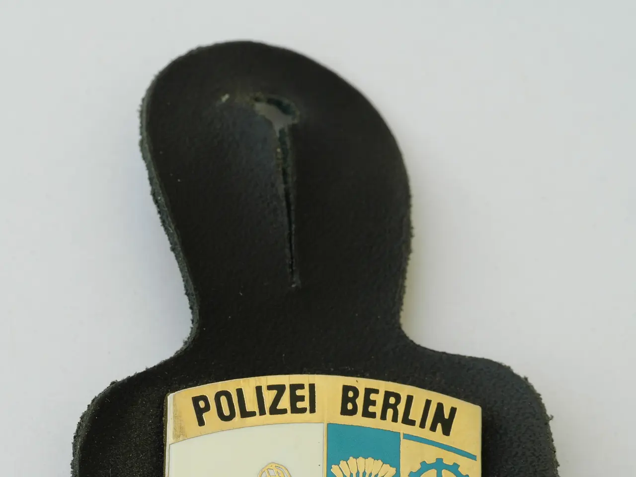 The image shows a police badge with the words "Police Berlin" on it, placed on a surface. The badge...