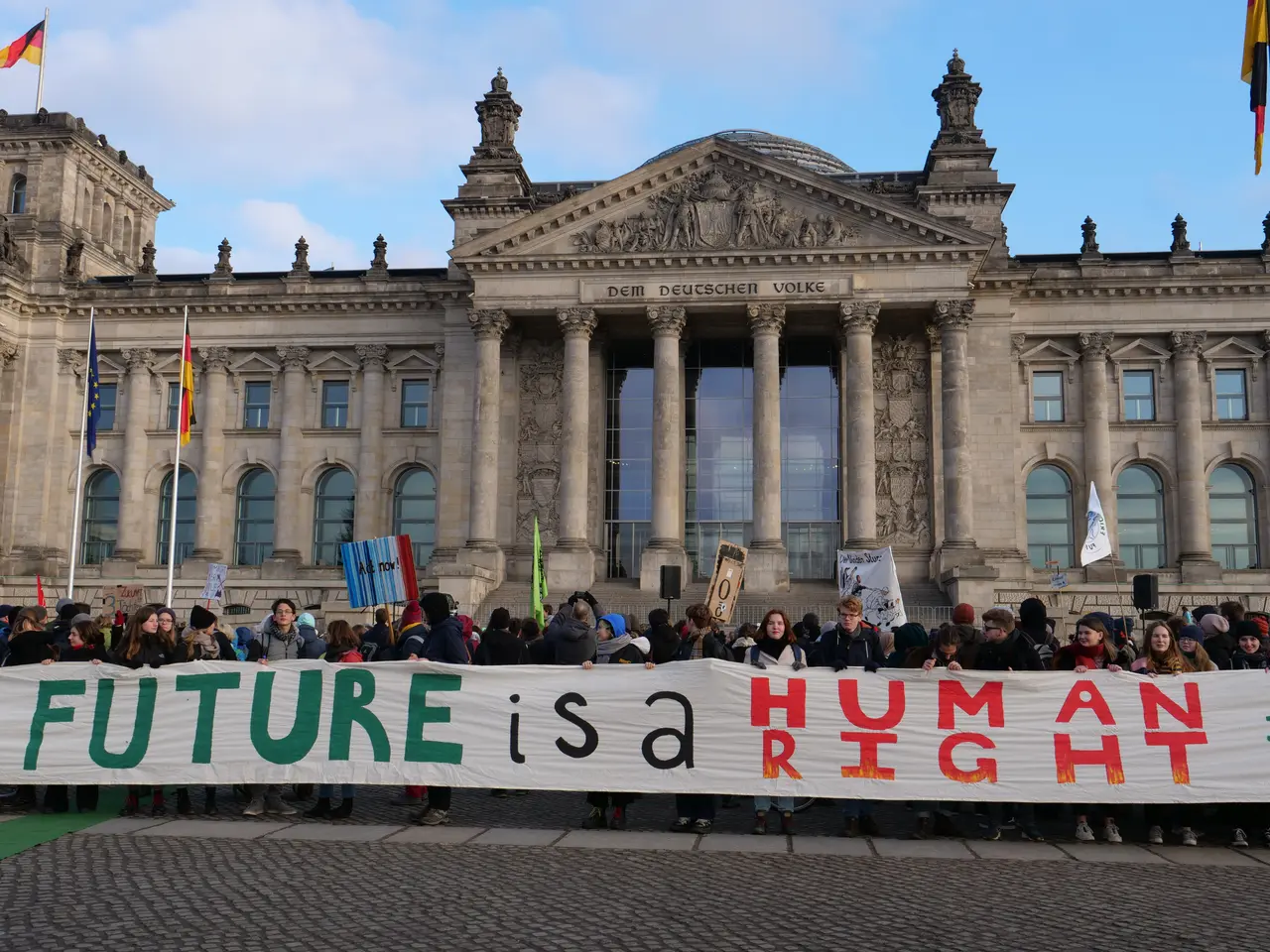The image shows a group of people holding a banner that reads "Future is a Human Right" in front of...