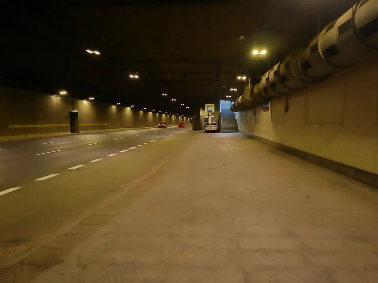 The image shows a long tunnel with cars driving through it at night. On the right side of the...