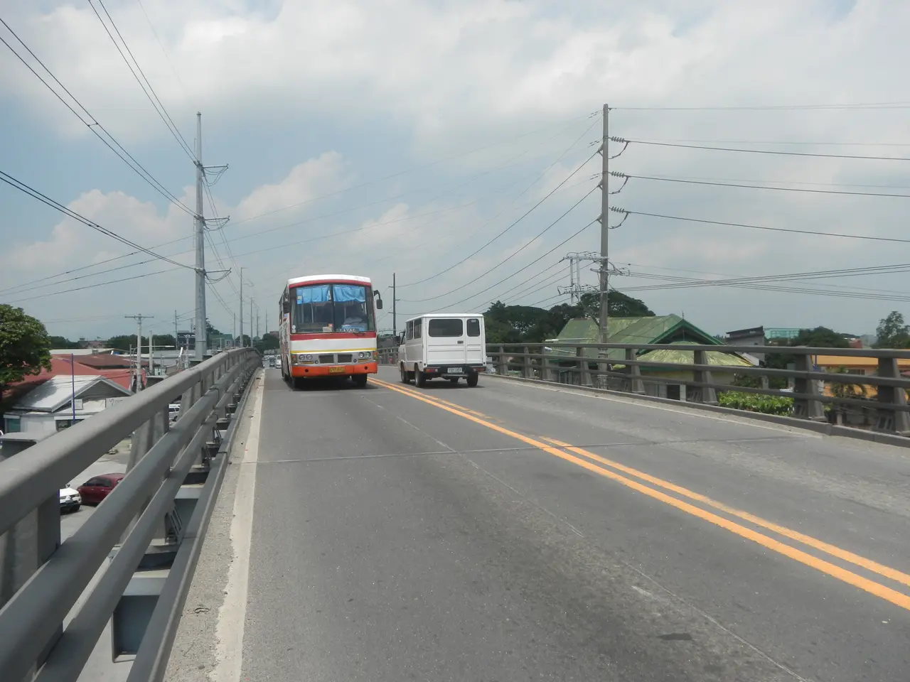 The image shows two buses driving across a bridge with railings on either side. In the background,...