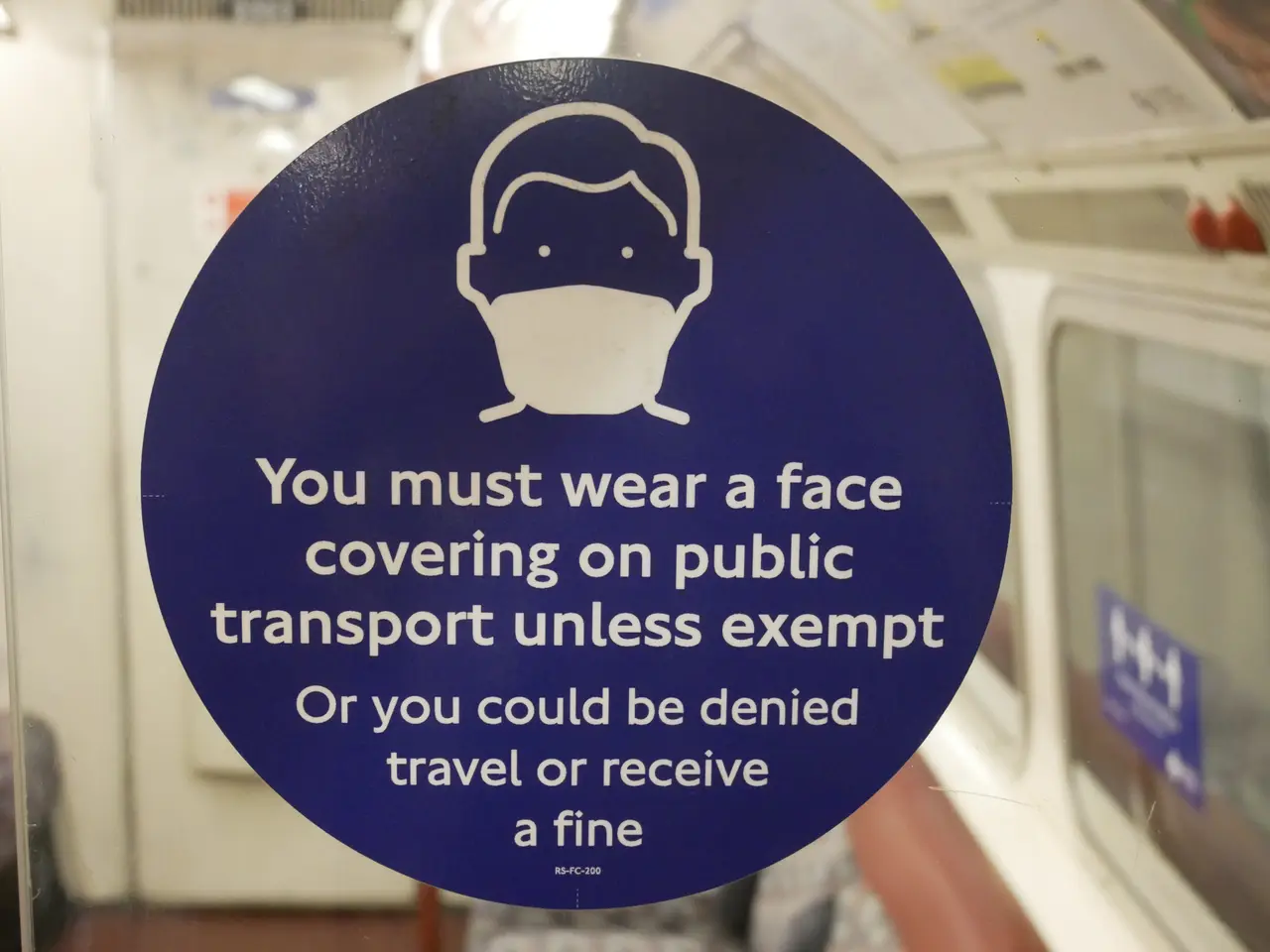The image shows a sign on the door of a train that reads "You must wear a face covering on public...