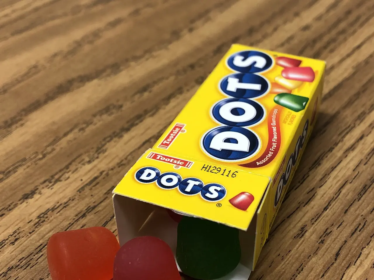 The image shows a box of colorful gummy bears sitting on top of a wooden table. The box is labeled...
