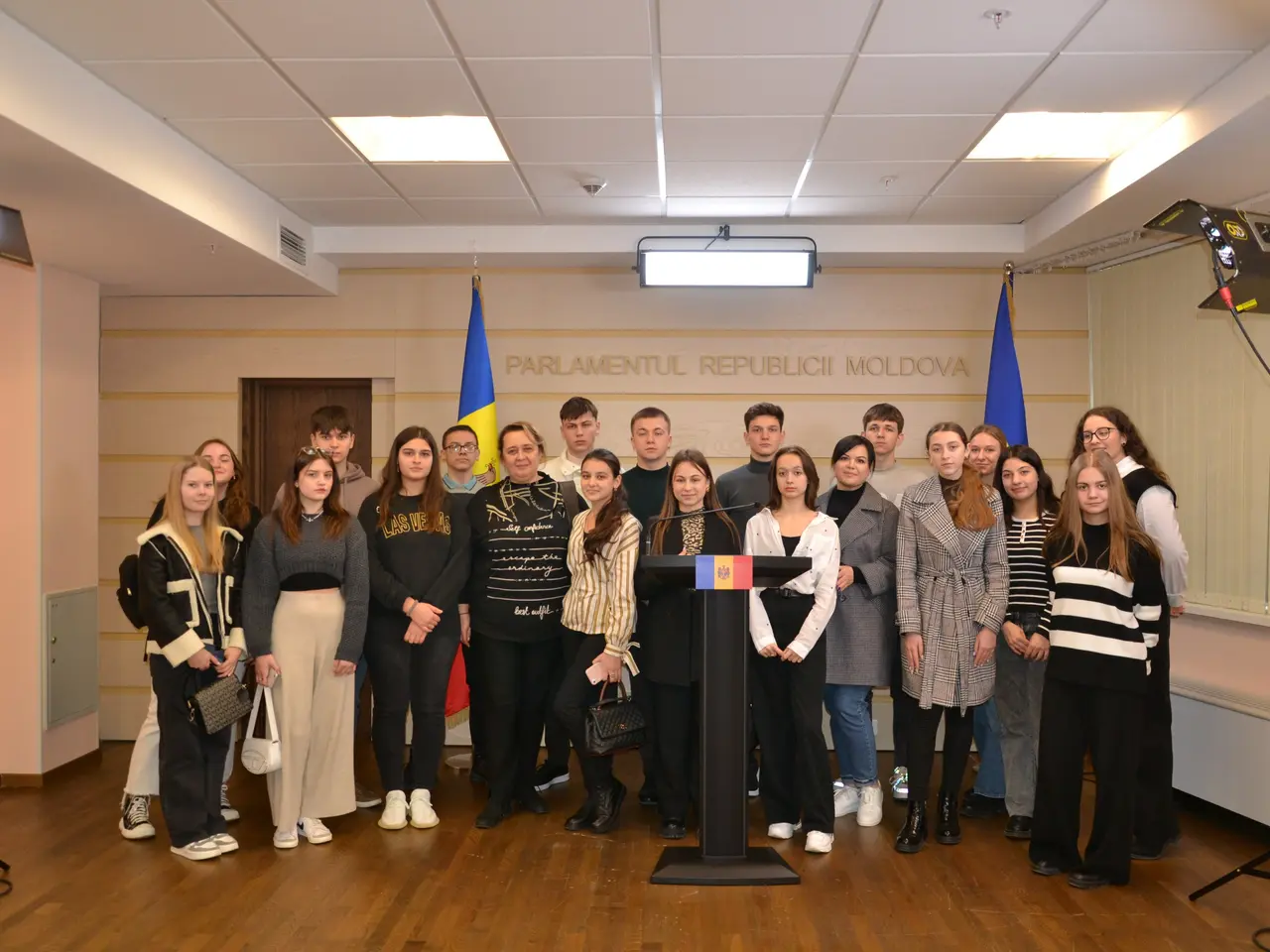 The image shows a group of people standing in front of a podium with a microphone, surrounded by...