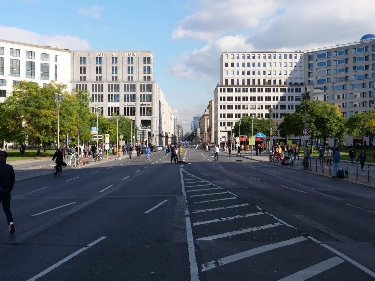 The image shows a bustling city street in Berlin, Germany, with people walking and riding bicycles...