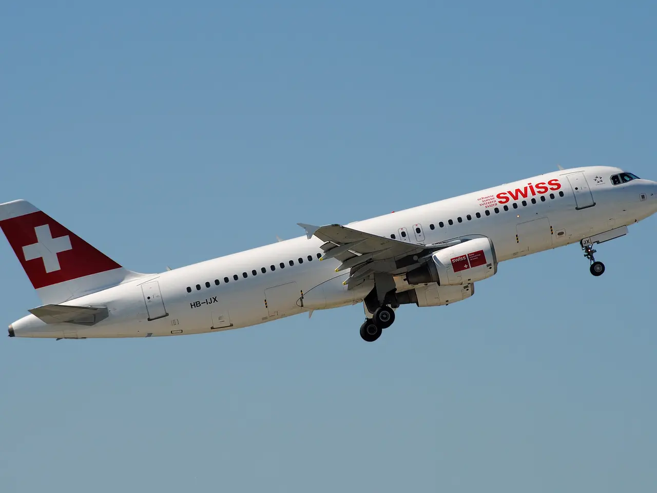 The image shows a Swiss Airlines Airbus A320-200 in flight, with its white and red livery standing...