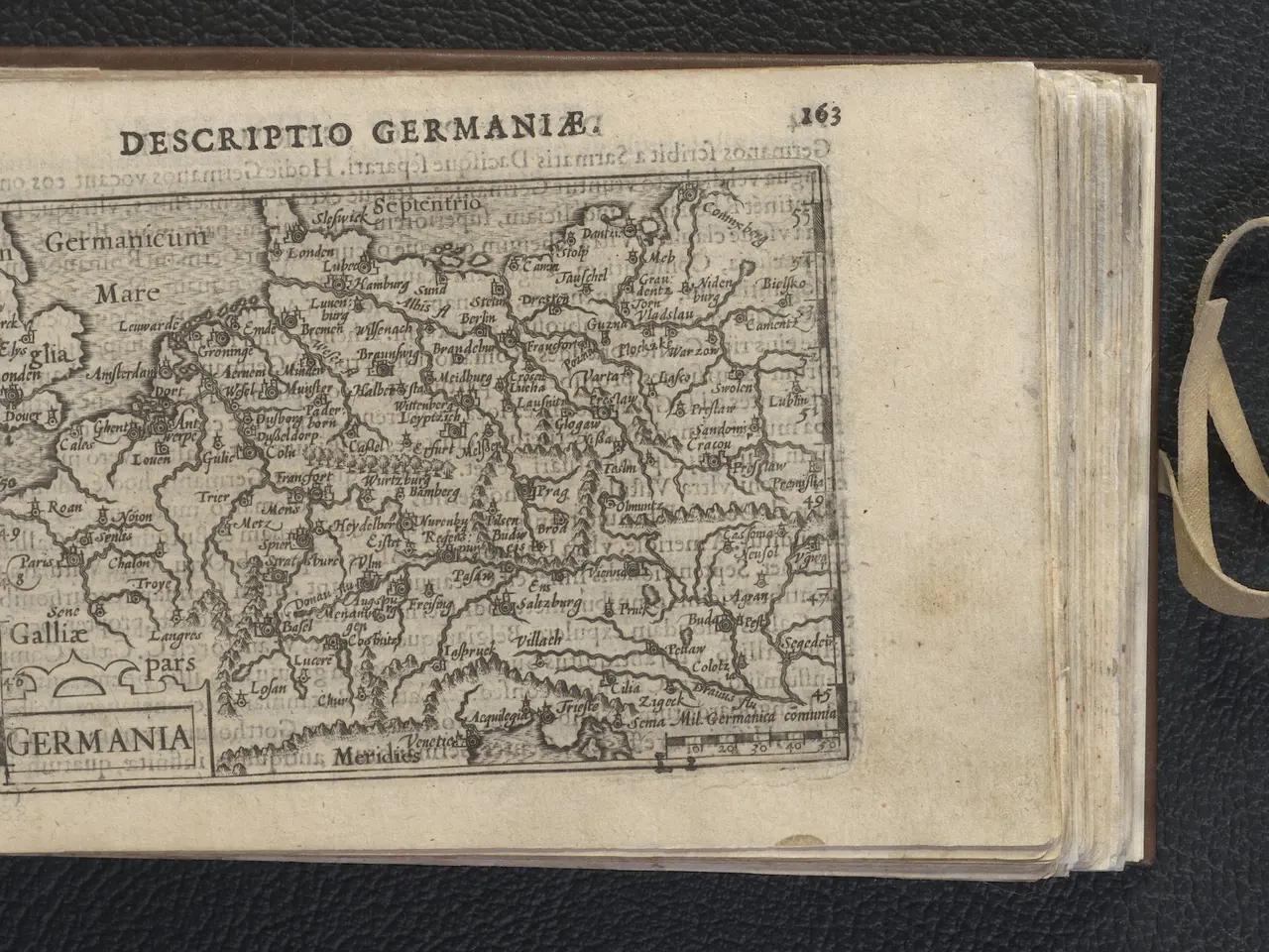 The image shows an open book with a map of Germany on it, placed on a black surface. The book is...
