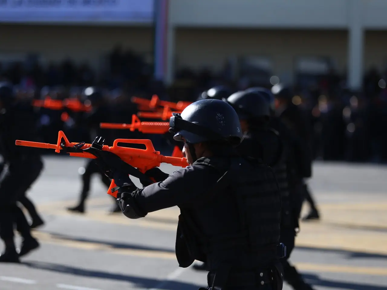 The image shows a group of police officers in riot gear marching down a street, wearing helmets and...