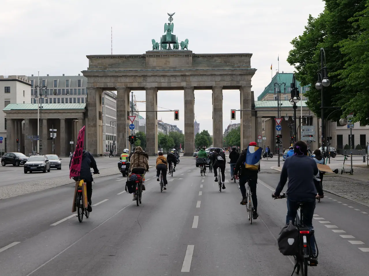 The image shows a group of people riding bicycles down a street in front of the Brandenburg Gate in...