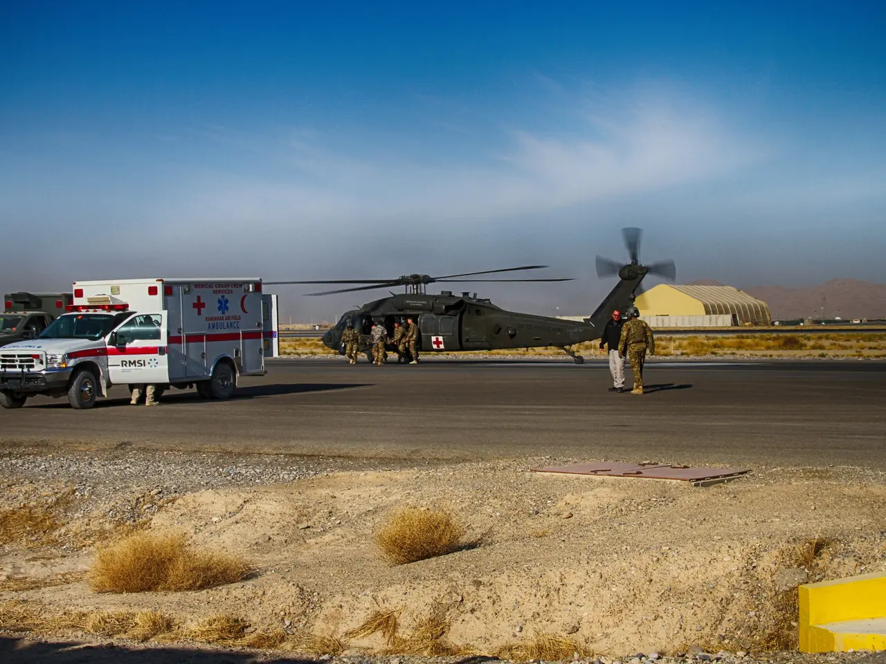 The image shows a helicopter parked on the side of a road next to an ambulance. There are people...