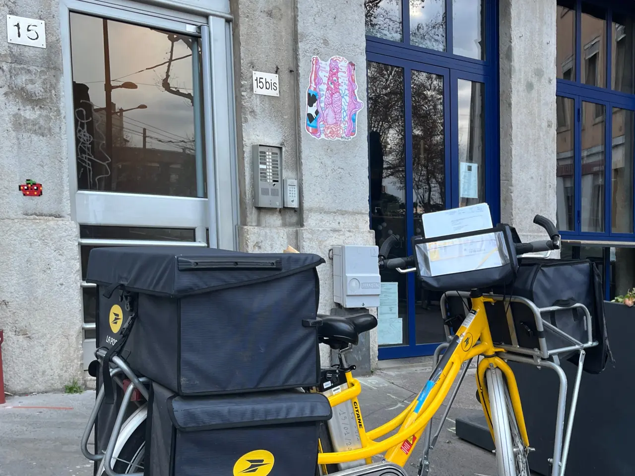 The image shows a yellow bicycle parked in front of a building with glass doors and windows. On the...