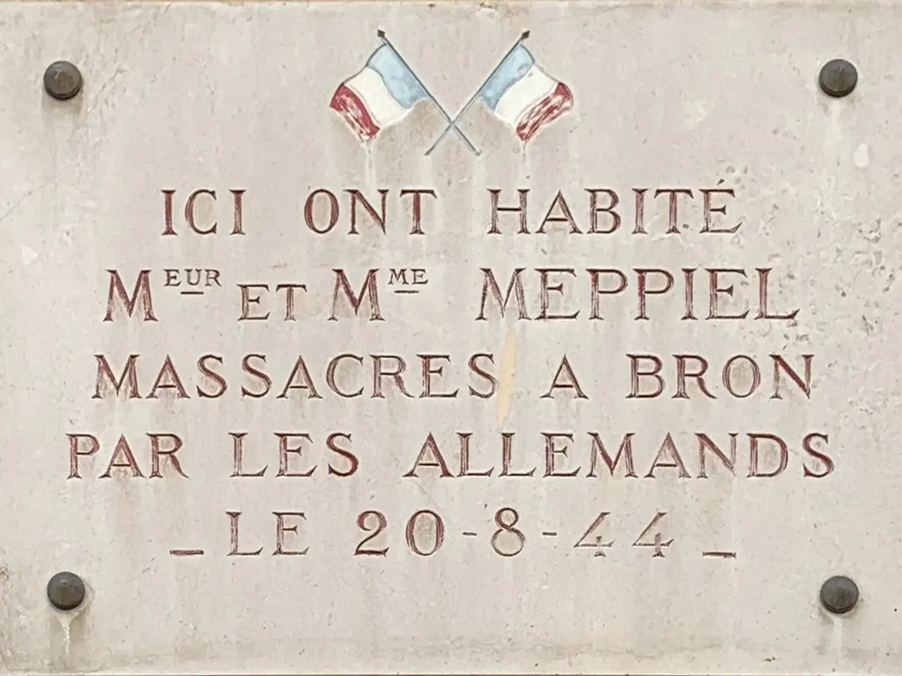 The image shows a plaque on the side of a building with two flags on it. The plaque is made of...