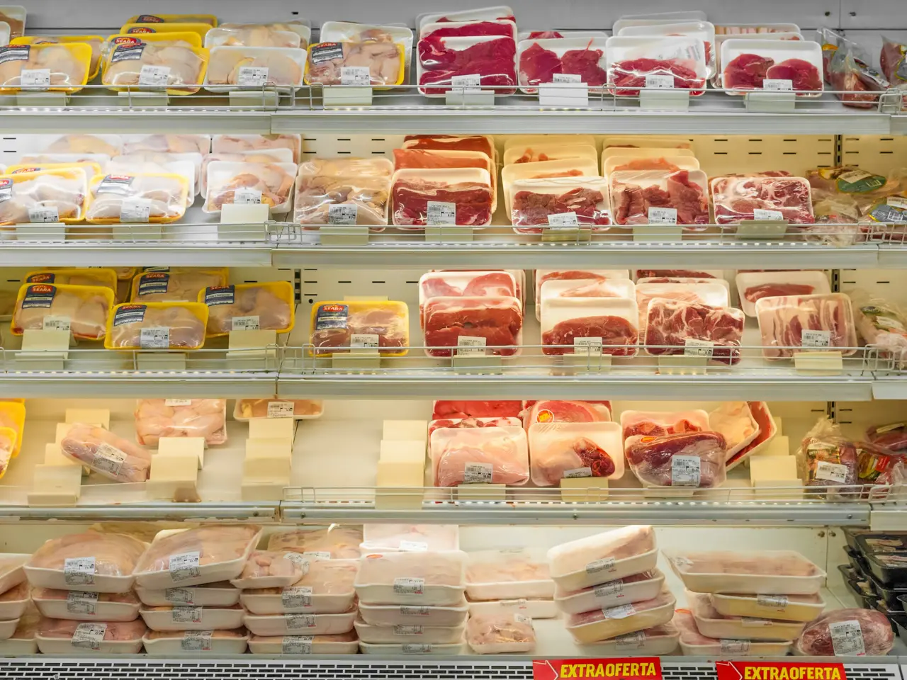 The image shows a grocery store filled with lots of different types of meat on the shelves, with...