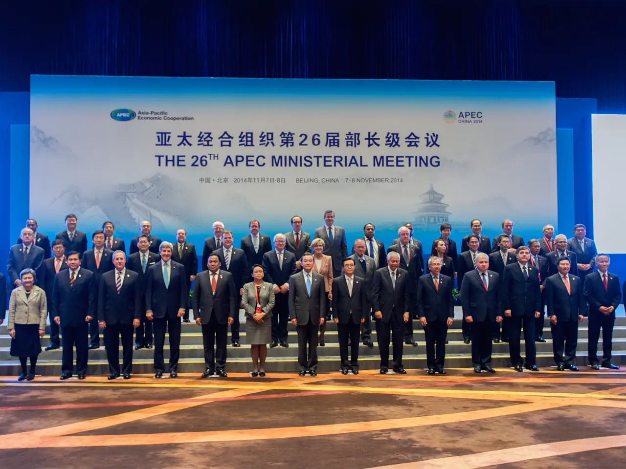 The image shows a group of people standing on top of a stage, wearing blazers, ties, shirts, and...