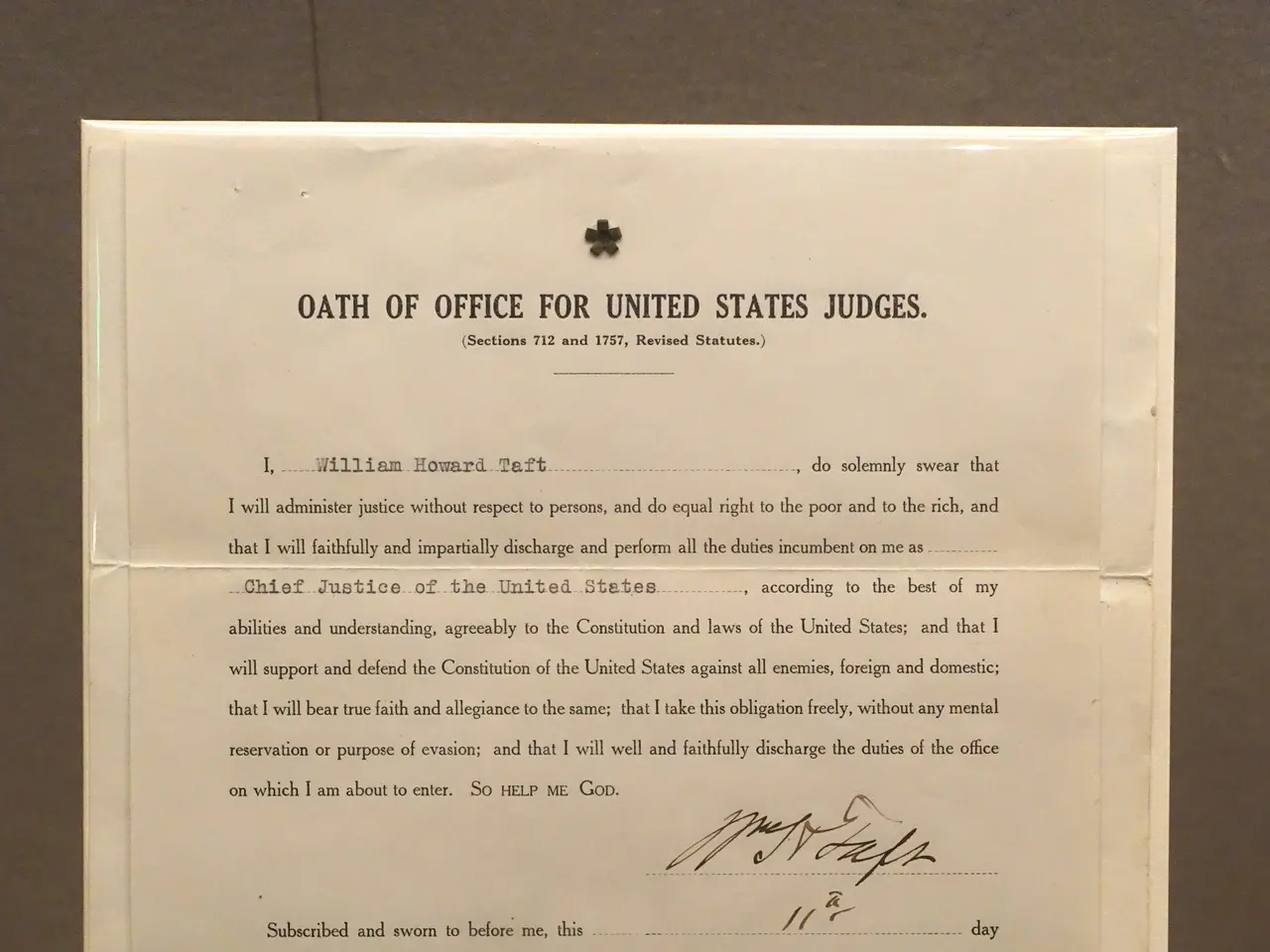 The image shows a paper with text on it placed on a table in front of a wall. The text reads "Oath...