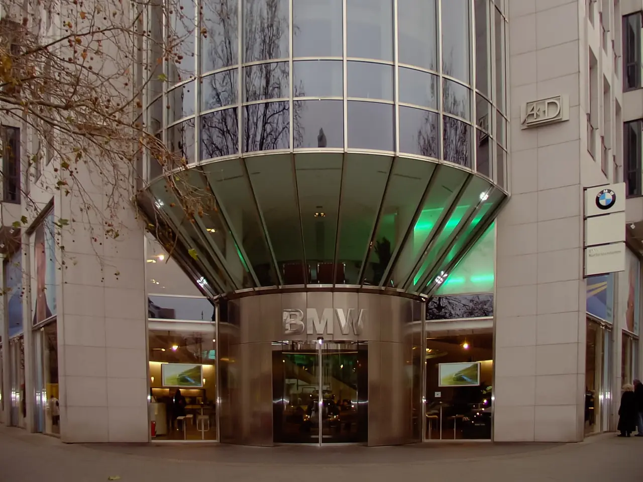 The image shows the BMW headquarters in Frankfurt, Germany. It is a large building with glass walls...