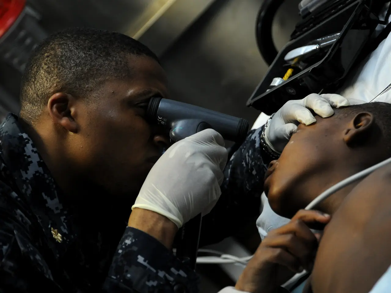 The image shows a man in a military uniform getting his eyes examined by a doctor. The doctor is...