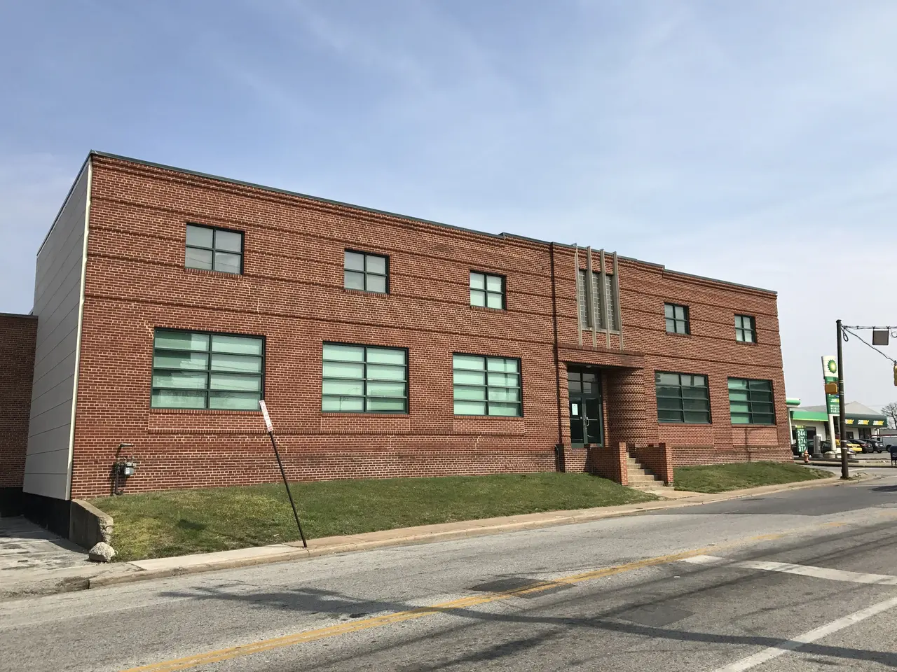 The image shows a large brick building on the corner of a street, with glass windows, steps with...
