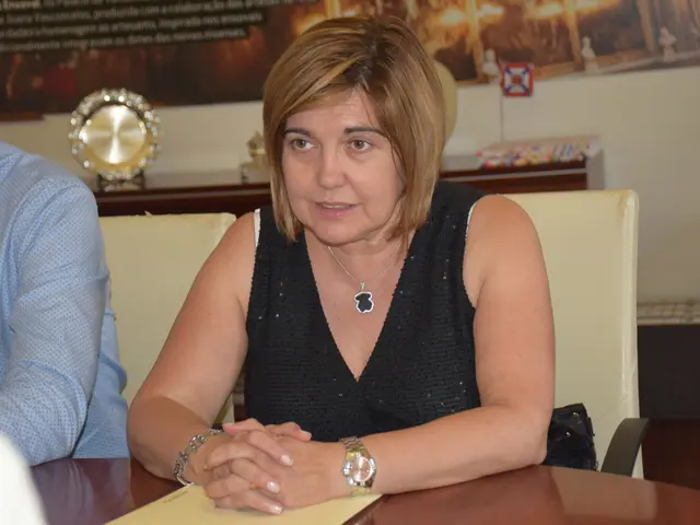 In this picture there is a woman wearing black top, sitting on the chair and looking straight....