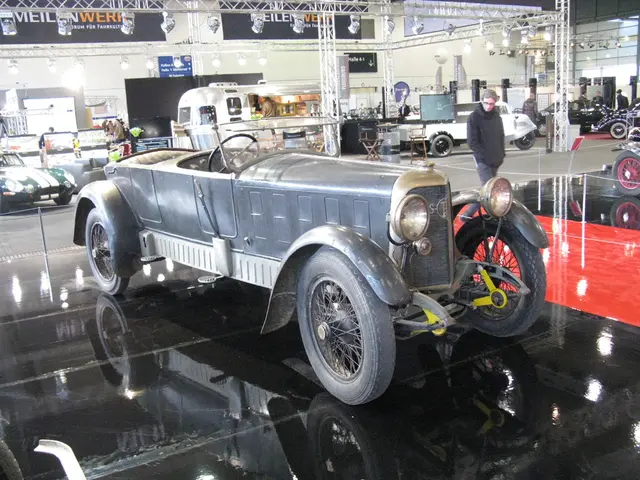 In this image there is a car on the floor. In the background there are so many cars parked one...