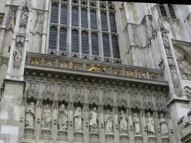 In the image there is a building with walls, glass windows, pillars, sculptures, arch and some...