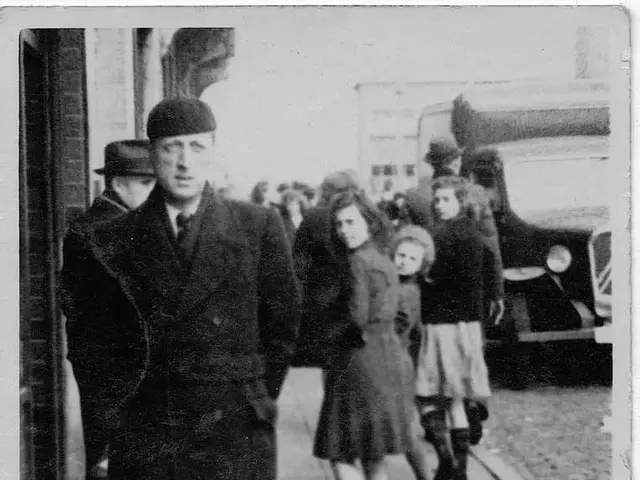 Black and white picture. Here we can see people and vehicle. Few people wore hats. Far there is a...