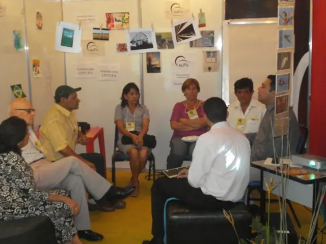 In this image there are a few people sitting in chairs discussing with each other, behind them...