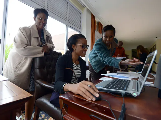 There is a woman sitting on the chair at the table and working on the laptop beside it there are...